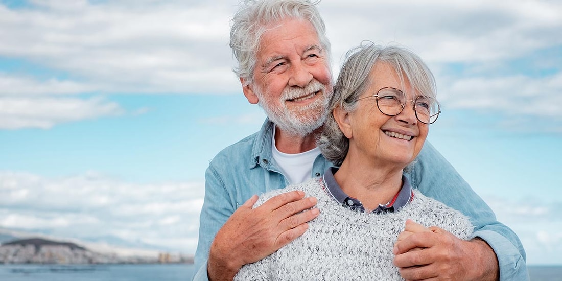 Et eldre par står ved sjøen og holder rundt hverandre, til illustrasjon for Seniorlån