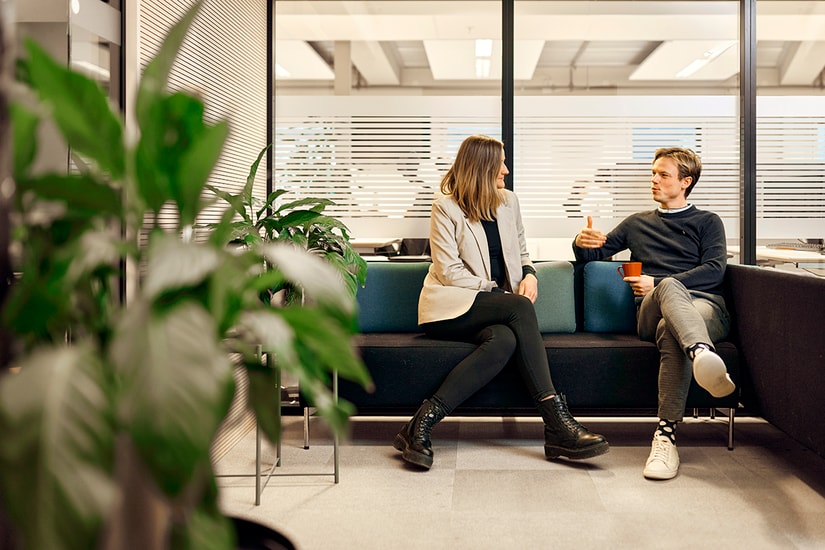 To ansatte i BN Bank sitter i en sofa med en kaffekopp og snakker, til illustrasjon for bedriftskunde i BN Bank