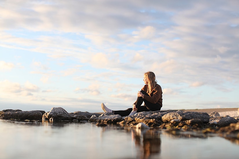 Ung jente sitter på fjærsteinene og ser utover havet