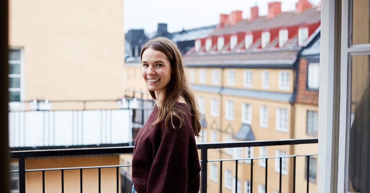 Ung jente står på en balkong og smiler, til illustrasjon for førstegangskjøp av bolig