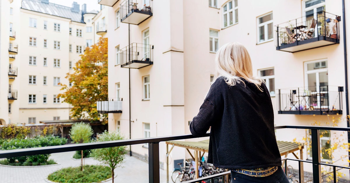 Dame på balkong ser utover bygård, til illustrasjon for selveier, andel og aksjeleilighet