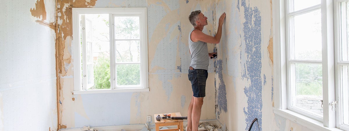 Mann skraper vekk tapet på vegg, til illustrasjon for kjøpe oppussingsobjekt