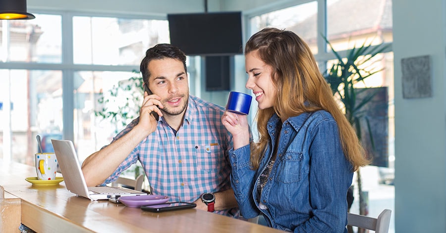 Par sitter i kjøkkenet med pc og mobil, til illustrasjon for å kuppe bolig