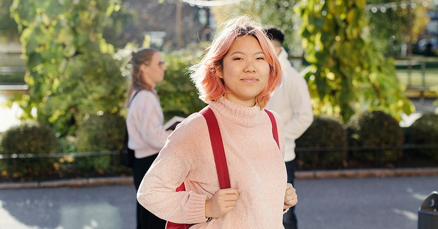 Jente med rosa hår står ute med en rød skolesekk, til illustrasjon for studentbudsjett