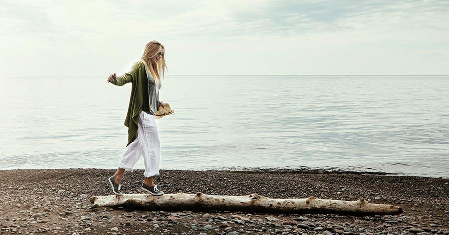 Dame balanserer på stokk ved stranden, til illustrasjon for feriepenger