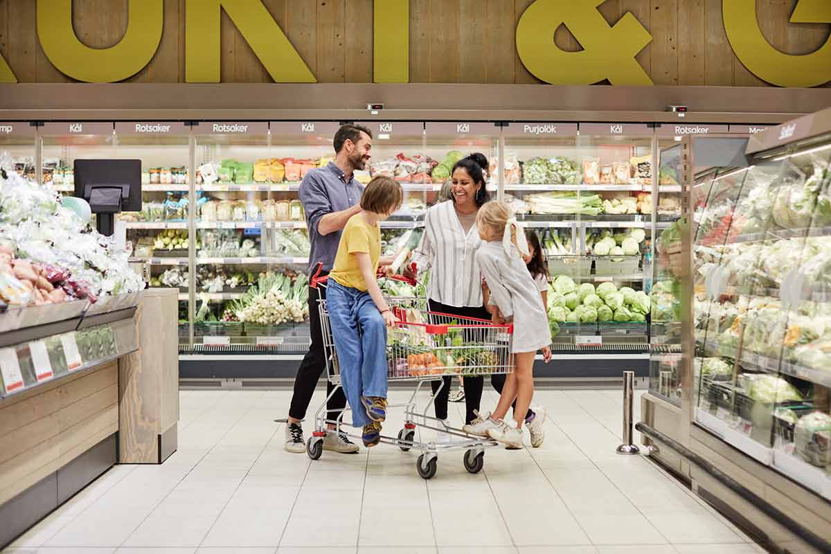 Mann, kvinne og to barn i en matbutikk med en handlevogn, til illustrasjon for hvordan spare penger i hverdagen