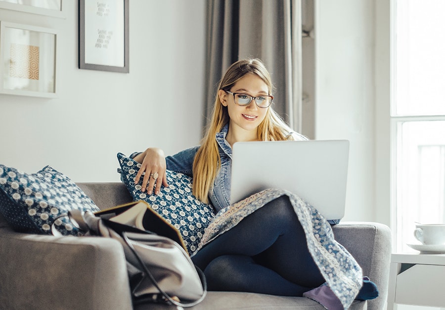 Kvinne sitter på sofaen med datamaskin i fanget, til illustrasjon for sikkerhet på nett