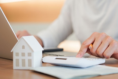 Mann sitter ved bord og jobber på PC og skriver på kalkulator, til illustrasjon for refinansiere forbruksgjeld