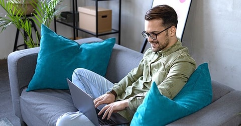 Mann sitter i sofa og jobber på PC, til illustrasjon for hvordan spare penger