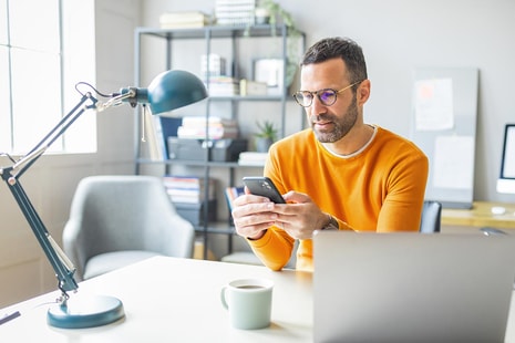 Mann med laptop ser på mobilen sin, illustrasjon til pensjonssparing