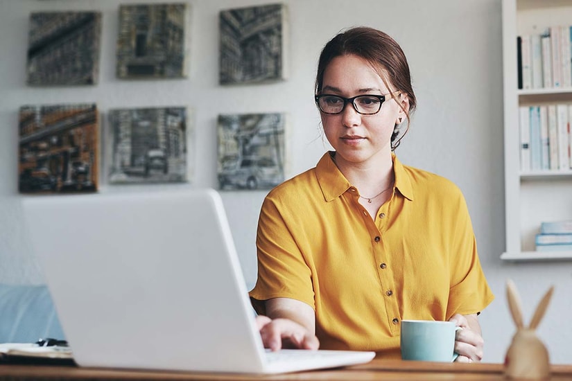 Dame med kaffekopp sitter og jobber på en PC, til illustrasjon for eFaktura