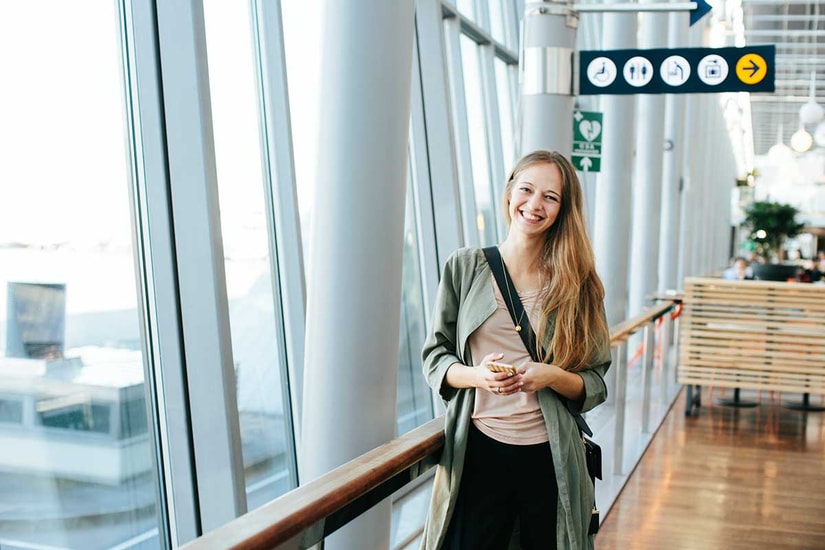 Jente står på flyplassen med mobilen i hånda, til illustrasjon for mobilbank
