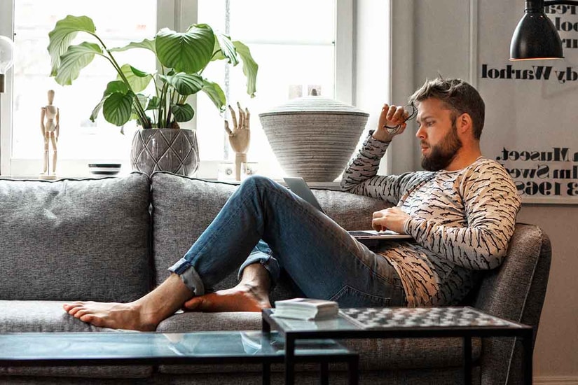 Mann sitter på sofaen og ser på laptop, til illustrasjon for nettbank