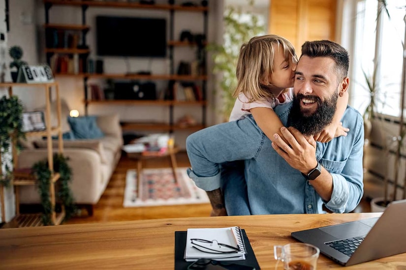 Mann sitter og jobber med et barn som klatrer på ryggen, til illustrasjon for fastrentelån