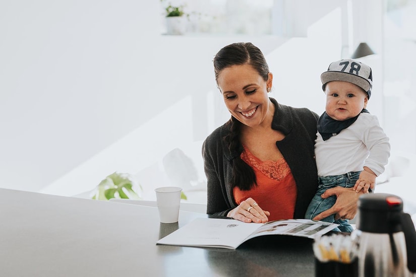 Kvinne holder et barn og ser på prospekter for å kjøpe ny bolig