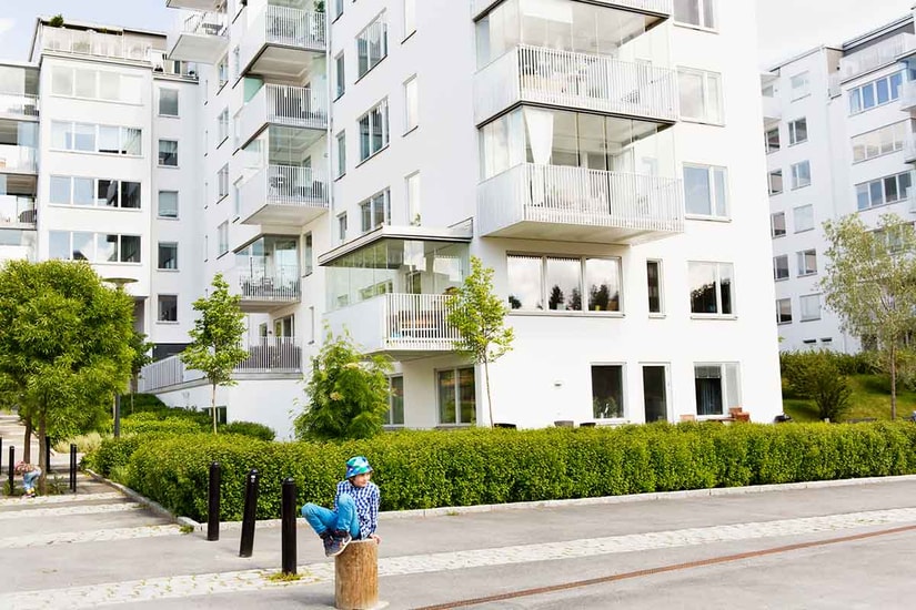 Gutt med bøttehatt sitter på en stokk fremfor en boligblokk, til illustrasjon for sekundærbolig