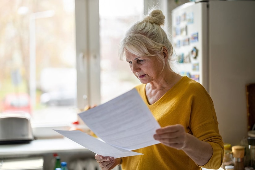 Eldre dame står på kjøkkenet og holder to dokumenter, til illustrasjon for utleie av bolig