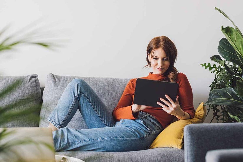 Dame sitter i sofa og leser på nettbrett, til illustrasjon for logg inn i bn bank