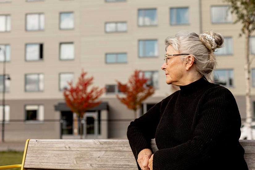 Eldre kvinne sitter på en benk utenfor en boligblokk, til illustrasjon for økonomi for eldre