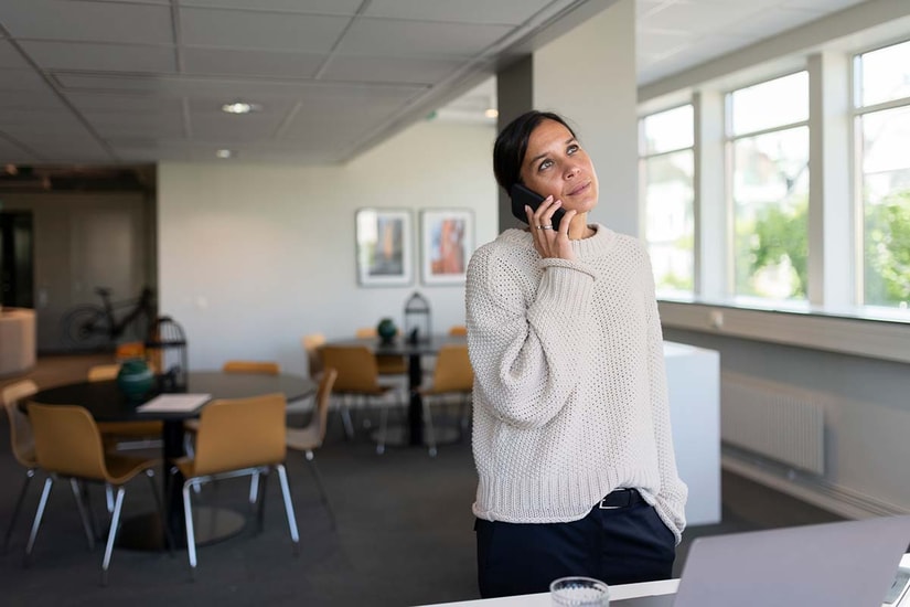 Dame står i et lokale med bord og stoler bak seg og snakker i telefonen, til illustrasjon for NIBOR-konto