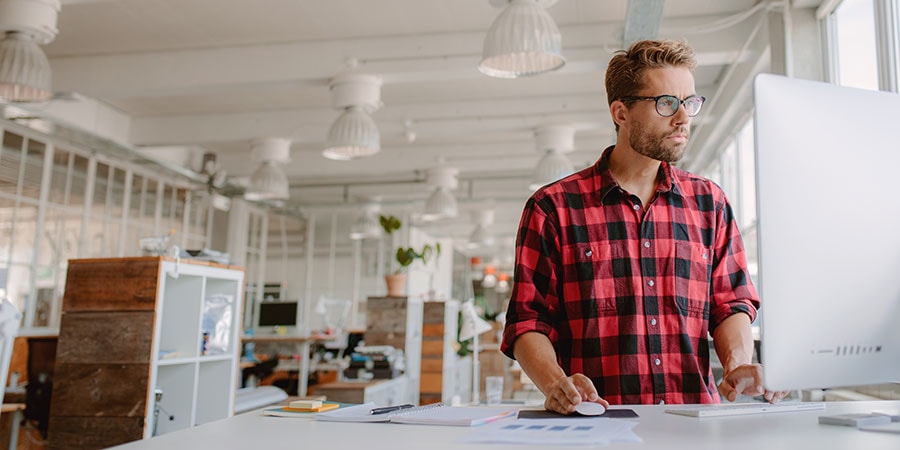 Mann i rutete skjorte ser på mac skjerm, til illustrasjon for bankkort for bedrift