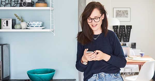 Kvinne lener seg mot vegg og sjekker mobiltelefonen, til illustrasjon for betaling