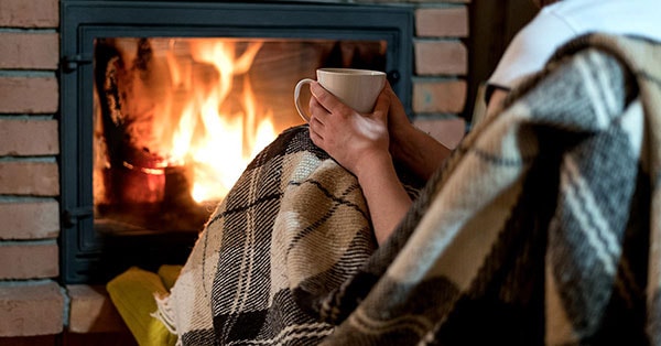 Dame sitter foran peis med en kopp i handa, til illustrasjo for energieffektivisere bolig