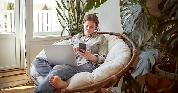 Dame slapper av i stolen med mobil og pc, til illustrasjon for boliglånsrente