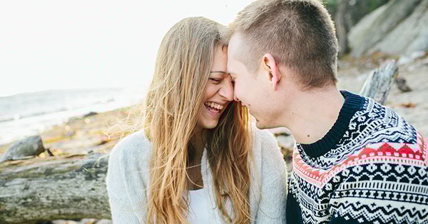 Par sitter på en strand og ler, til illustrasjon for å kjøpe seg inn i bolig
