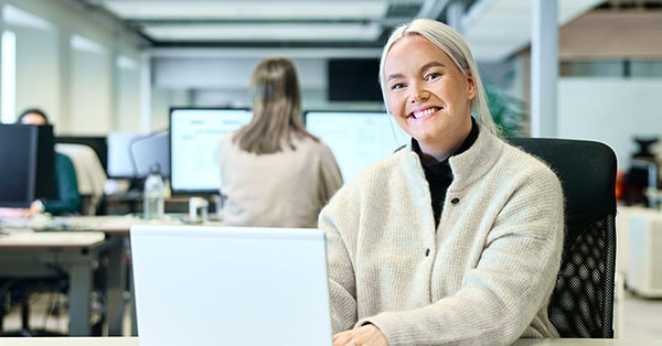 Boliglånsrådgiver Emilie sitter på kontoret og smiler med ansatte bak seg