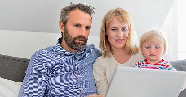 Mann, kvinne og barn sitter i sofa og ser på PC, til illustrasjon for spare eller låne