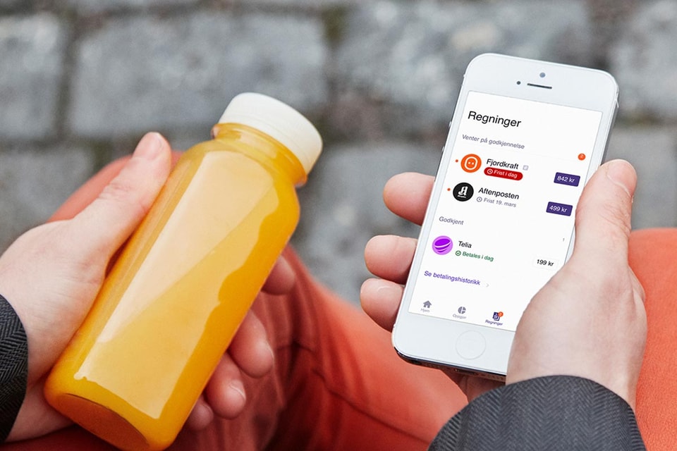 Mann sitter med en appelsinjuice i hånda og mobilen i den andre som du kan bruke til å betale regninger