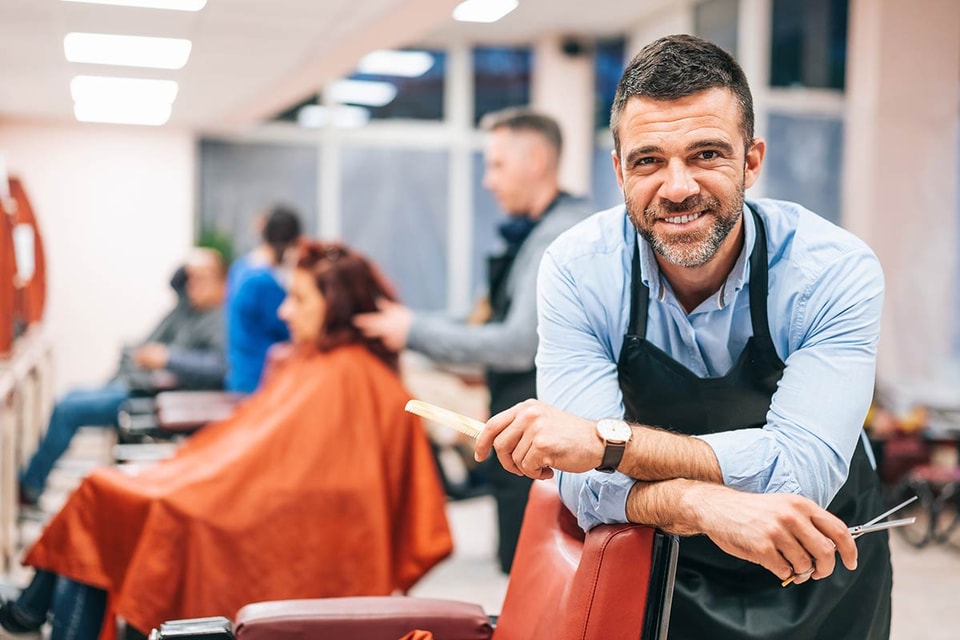 Frisør lener seg over frisørstol i sin egen bedrift, til illustrasjon for driftskonto