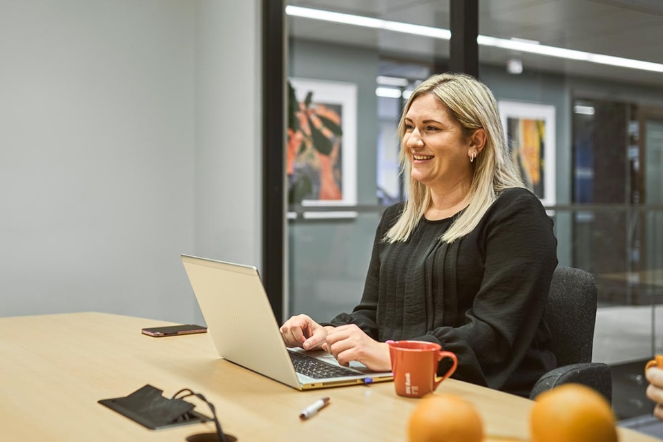 Bedriftsrådgiver Ailin sitter på møterom i BN Bank sine lokaler med en datamaskin fremfor seg, til illustrasjon for bedriftskonto