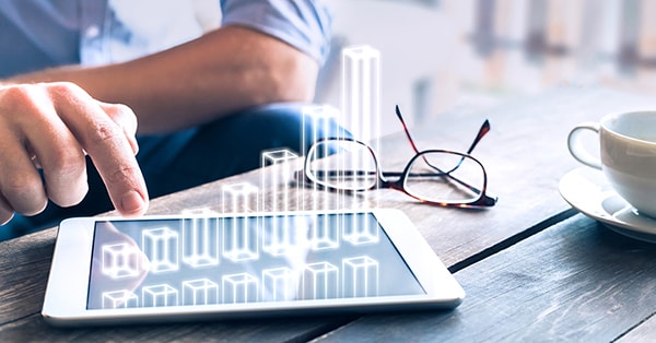 Mann sitter å plotter inn tall på nettbrettet, til illustrasjon for sparing til bedrift