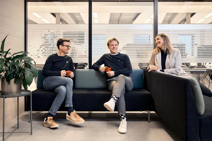 Tre personer sitter på en sofa i et kontor, smilende og jobber i BN Bank