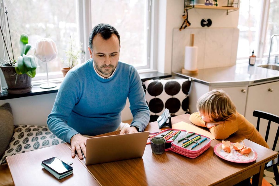 Far og barn sitter ved spisebordet og jobber på PC, til illustrasjon for reklamasjon